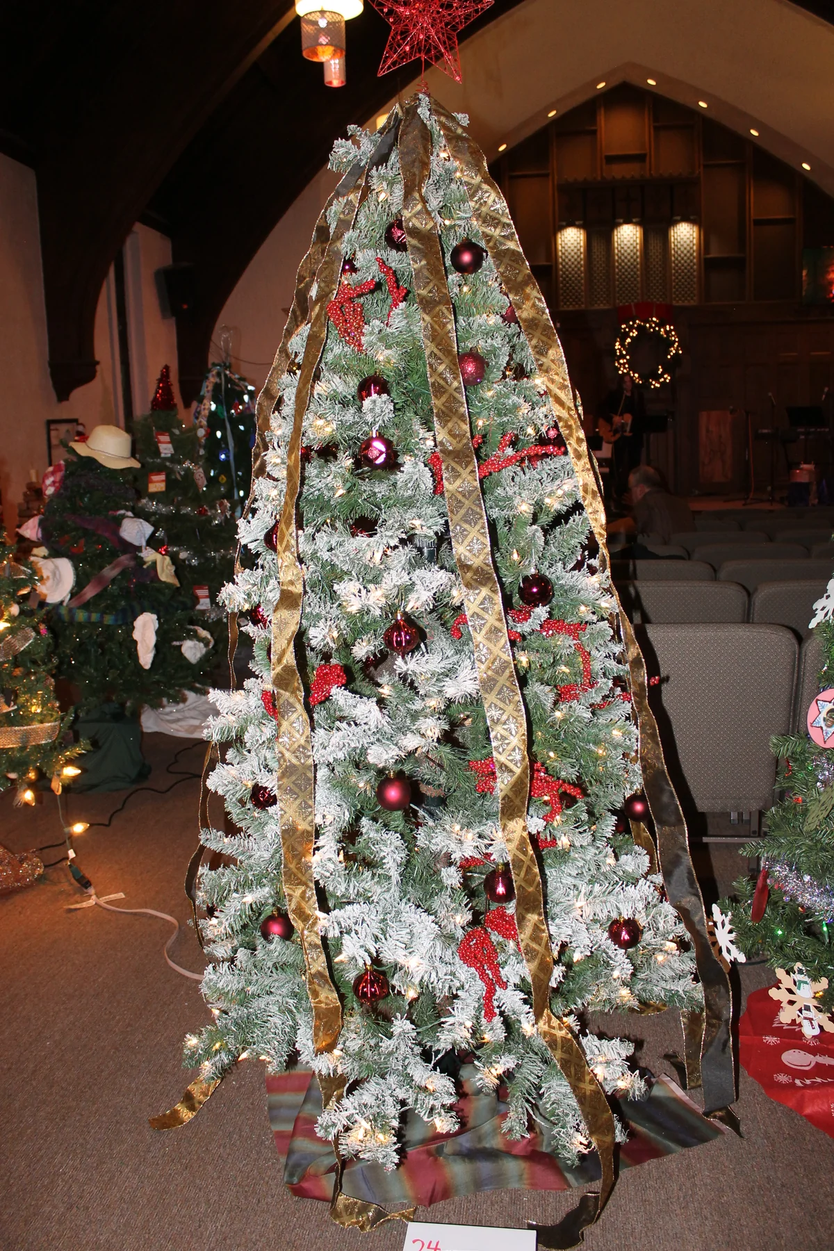 A snowy tree with red ornaments and long gold ribbon beneath a red star